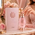 Zimaya Kibria Glory by Zimaya 100ml Women — Botol minyak wangi merah jambu dengan penutup bentuk mahkota dan perincian emas ros, bersebelahan kotak merah jambu bertekstur yang sepadan. Tangan bertindik sedang mencapai botol, berlatar belakang bunga lembut.