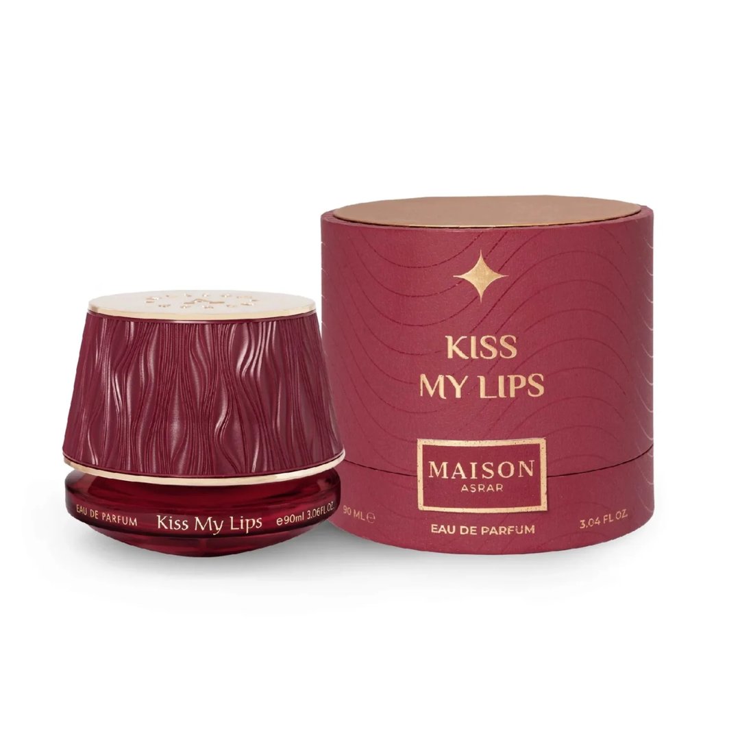 Maison Asrar Kiss My Lips by Maison Asrar 90ml EDP Unisex — Botol minyak wangi merah gelap bertekstur dengan penutup emas terletak di sebelah kotak silindernya yang sepadan, kedua-duanya mempunyai aksen dan tulisan emas.