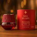 Maison Asrar Kiss My Lips oleh Maison Asrar 90ml EDP Unisex — Botol minyak wangi bertutup merah bertekstur dan kotak silinder sepadan dengan tulisan emas di atas permukaan kayu dengan lampu bokeh.