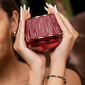 Maison Asrar Kiss My Lips by Maison Asrar 90ml EDP Unisex — Tangan wanita berkuku putih panjang memegang botol minyak wangi merah bertekstur dengan aksen emas, menunjukkan label 'Kiss My Lips' dan isipadu.