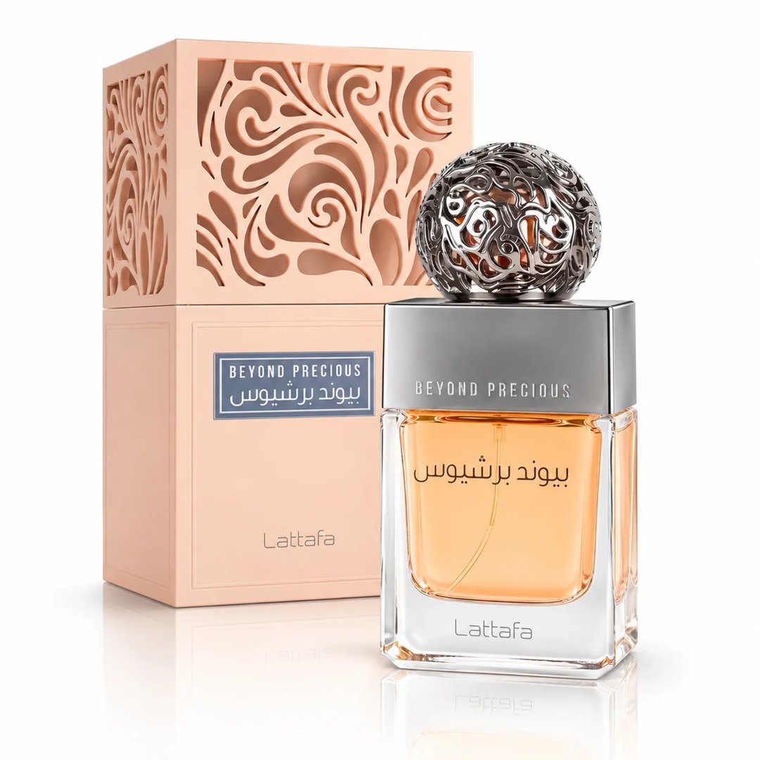 Lattafa Beyond Precious by Lattafa 100ml EDP Women — Botol minyak wangi kaca jernih berisi cecair oren, bertutup perak berukir, terletak bersebelahan kotak berwarna pic dengan ukiran menarik. Bunga putih dan permukaan marmar melengkapkan suasana.