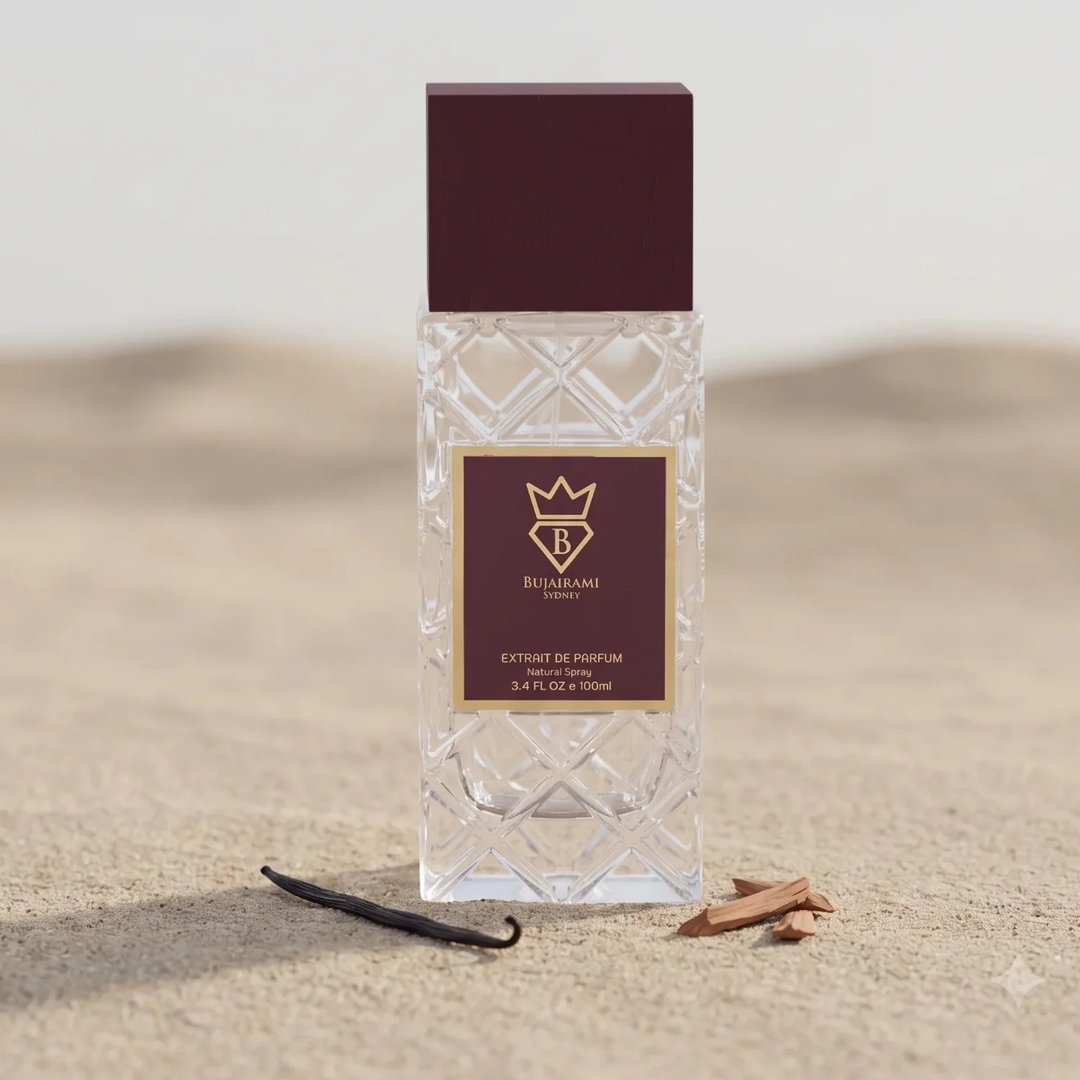 Bujairami Billion Dollar by Bujairami 100ml Extrait — Clear glass perfume bottle with a maroon cap, set on sand with a vanilla bean and sandalwood pieces.
