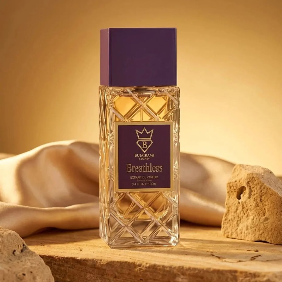 Bujairami Breathless by Bujairami 100ml Extrait — Clear faceted glass bottle with gold label, purple cap, on a wooden surface with draped silk and rocks.