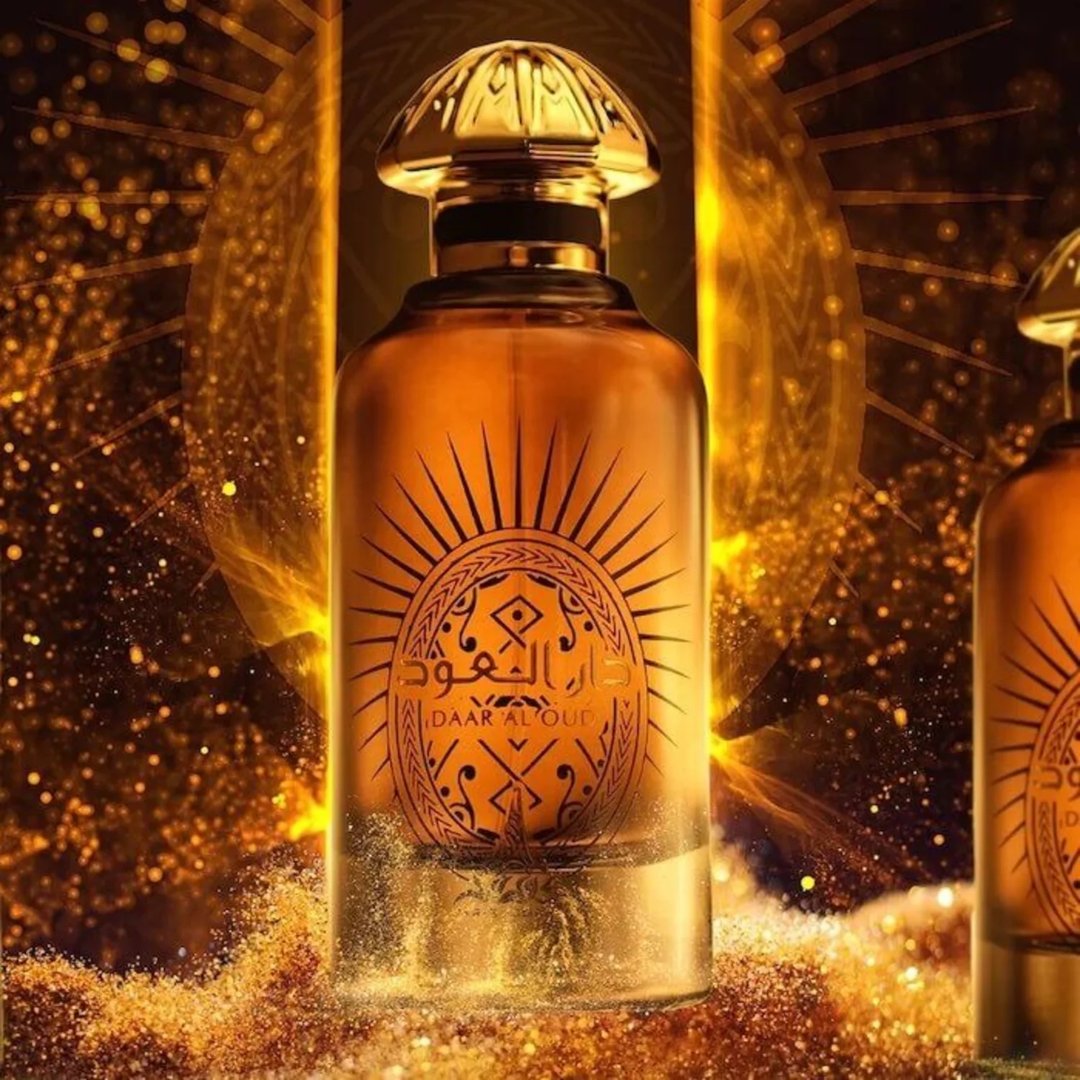 Paris Corner Daar Al Oud Intense 100ml — Amber glass perfume bottle with ornate sunburst label and gold cap, set against a shimmering golden bokeh background with scattered glitter. | Paris Corner Daar Al Oud Intense 100ml — Botol minyak wangi kaca ambar dengan label perincian sinaran matahari dan penutup emas