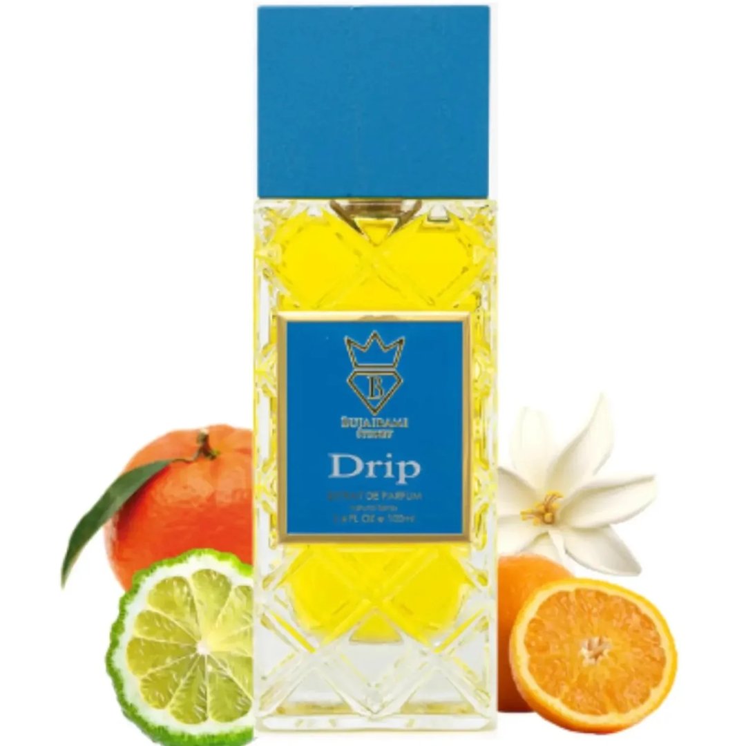 Bujairami Drip by Bujairami 100ml Extrait — Clear glass perfume bottle with yellow liquid, blue label with gold crown and 'B' logo, surrounded by citrus fruits and a white flower.
