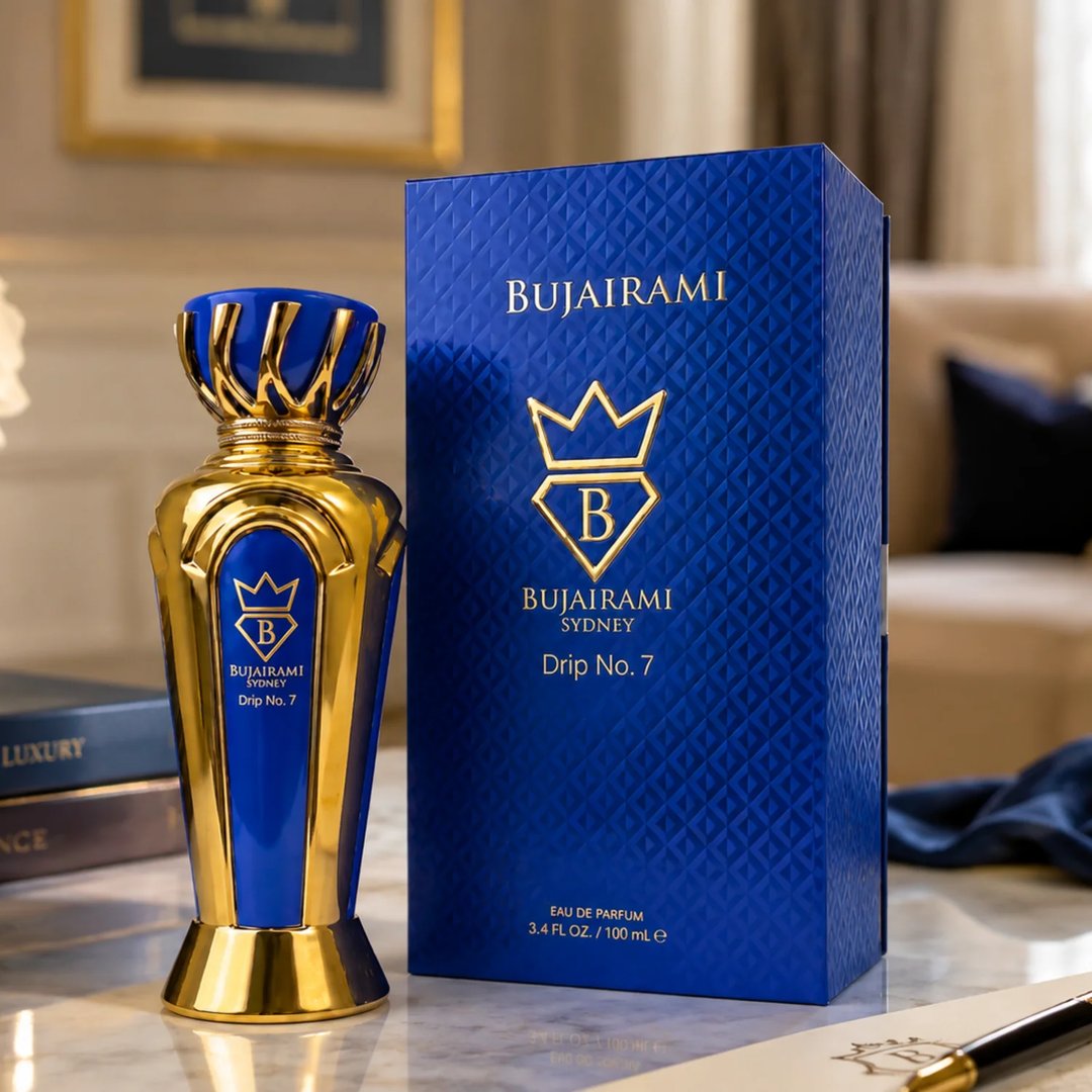 Bujairami Drip No. 7 — A tall, ornate gold and blue perfume bottle stands next to its matching blue textured box on a marble surface. Books are visible in the background.