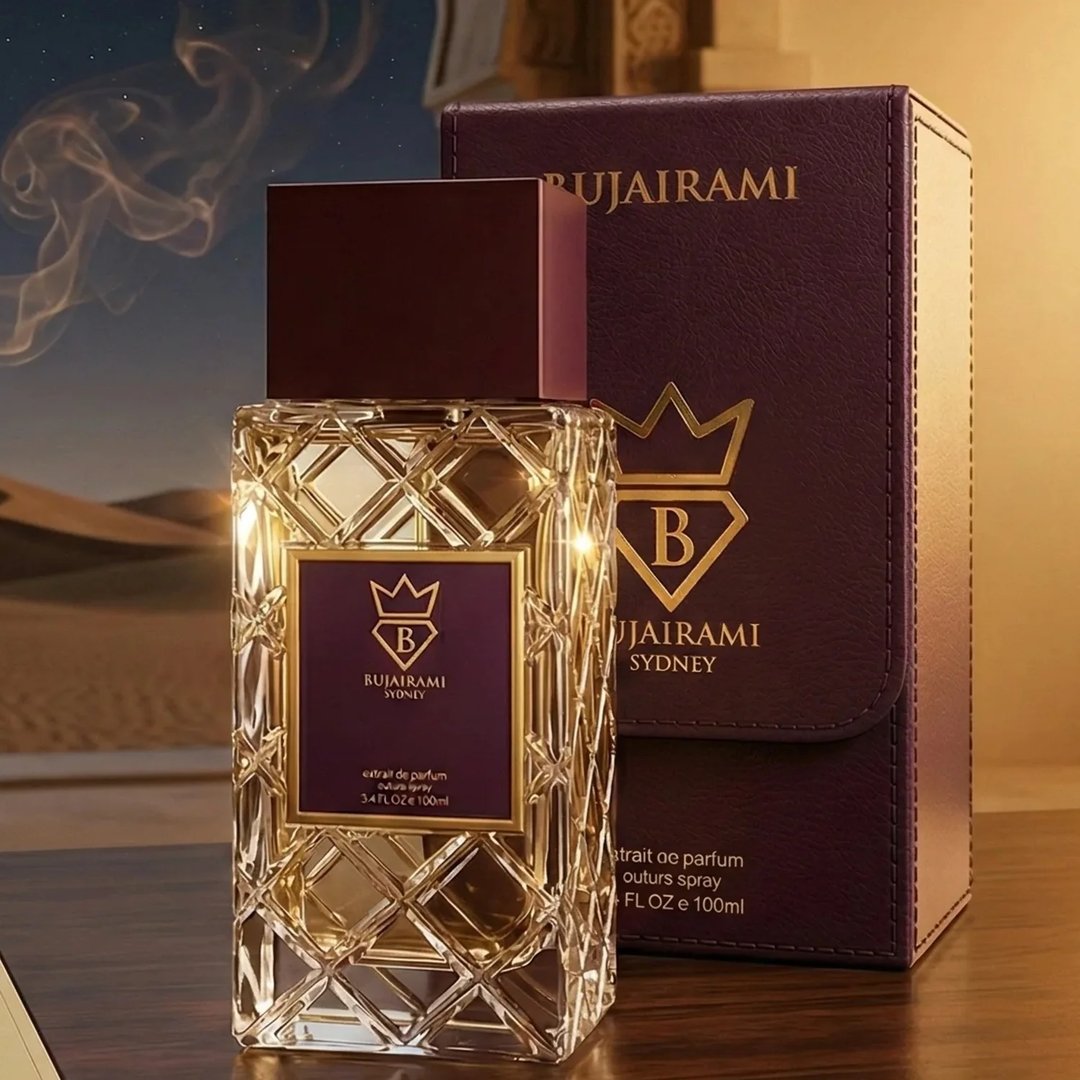 Bujairami Imperial Oud by Bujairami 100ml Extrait — Clear faceted glass bottle with gold accents and a deep purple label, next to its matching deep purple presentation box with gold crown logo, set against a desert landscape background with smoke wisps.