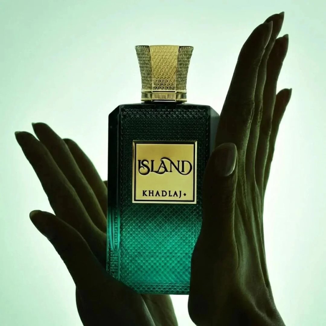 Khadlaj Island Extrait de Parfum 100ml by Khadlaj — A dark green, textured glass perfume bottle with a gold cap, held by two hands against a light green gradient background. | Khadlaj Island Extrait de Parfum 100ml by Khadlaj — Botol minyak wangi kaca bertekstur hijau gelap dengan penutup emas, dipegang oleh dua