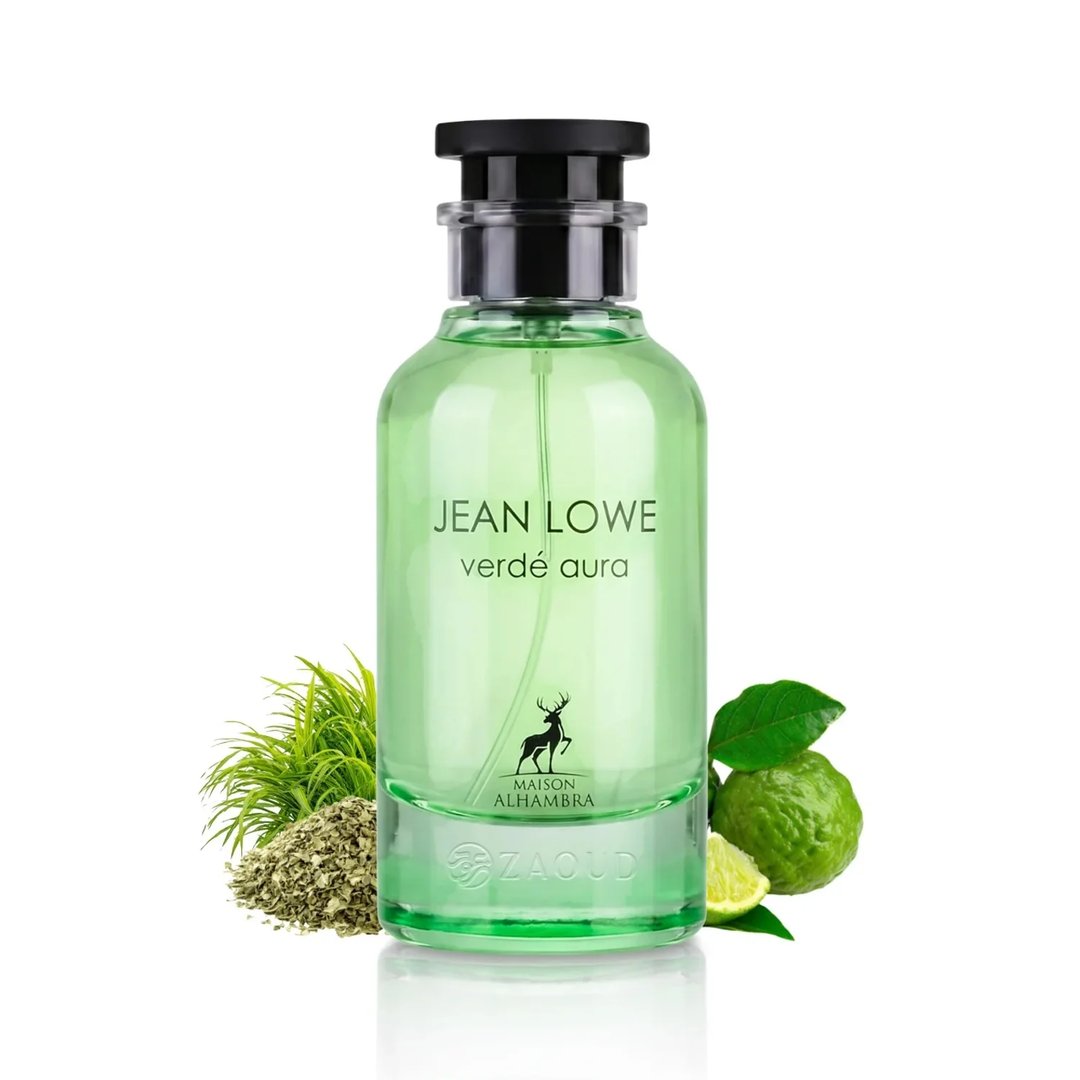 Maison Alhambra Jean Lowe Verde Aura — A green glass perfume bottle with a black cap, surrounded by fresh green grass, dried herbs, and a lime fruit. | Maison Alhambra Jean Lowe Verde Aura — Botol kaca hijau dengan penutup hitam, dikelilingi oleh rumput hijau segar, herba kering, dan buah limau.