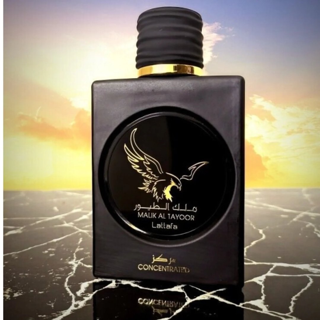 Lattafa Malik Al Tayoor Concentrated 100ml by Lattafa — Black square perfume bottle with a gold eagle emblem and Arabic text, set against a sunset sky and reflective marble surface. | Lattafa Malik Al Tayoor Concentrated 100ml by Lattafa — Botol minyak wangi hitam persegi dengan lambang helang emas dan teks Arab