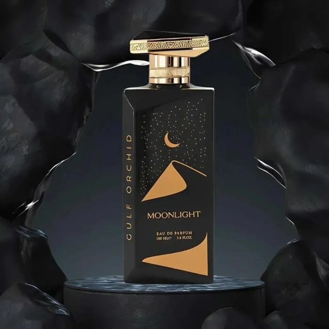 Gulf Orchid Moonlight Eau De Parfum 100ml by Gulf Orchid — A black perfume bottle with gold accents and a desert night scene on the label, displayed on a dark circular pedestal against a textured black background. | Gulf Orchid Moonlight Eau De Parfum 100ml by Gulf Orchid — Botol minyak wangi hitam dengan aksen emas