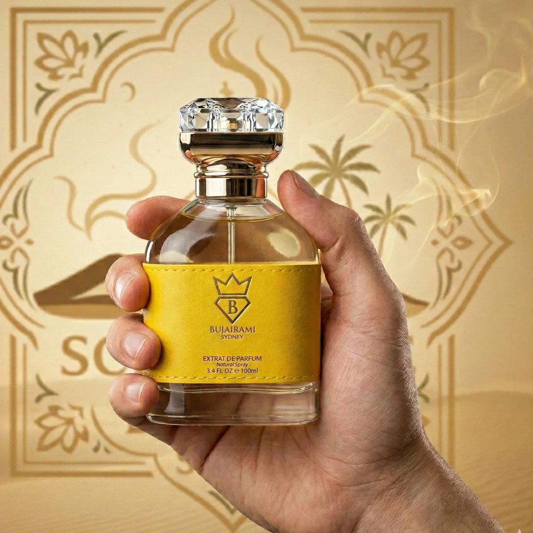 Bujairami Next Level by Bujairami 100ml Extrait — Hand holding a clear glass perfume bottle with a yellow textured band and a crystal-like cap, against a golden desert-themed background with palm trees and ornate patterns.