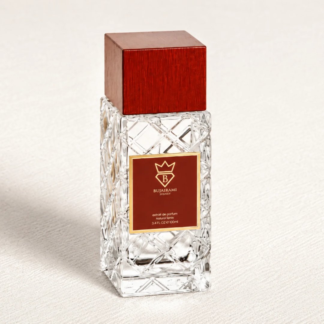 Bujairami Oud Money by Bujairami 100ml Extrait — Clear faceted glass bottle with a textured pattern, topped with a dark red wooden cap. A maroon label with gold trim features the brand logo and product details.