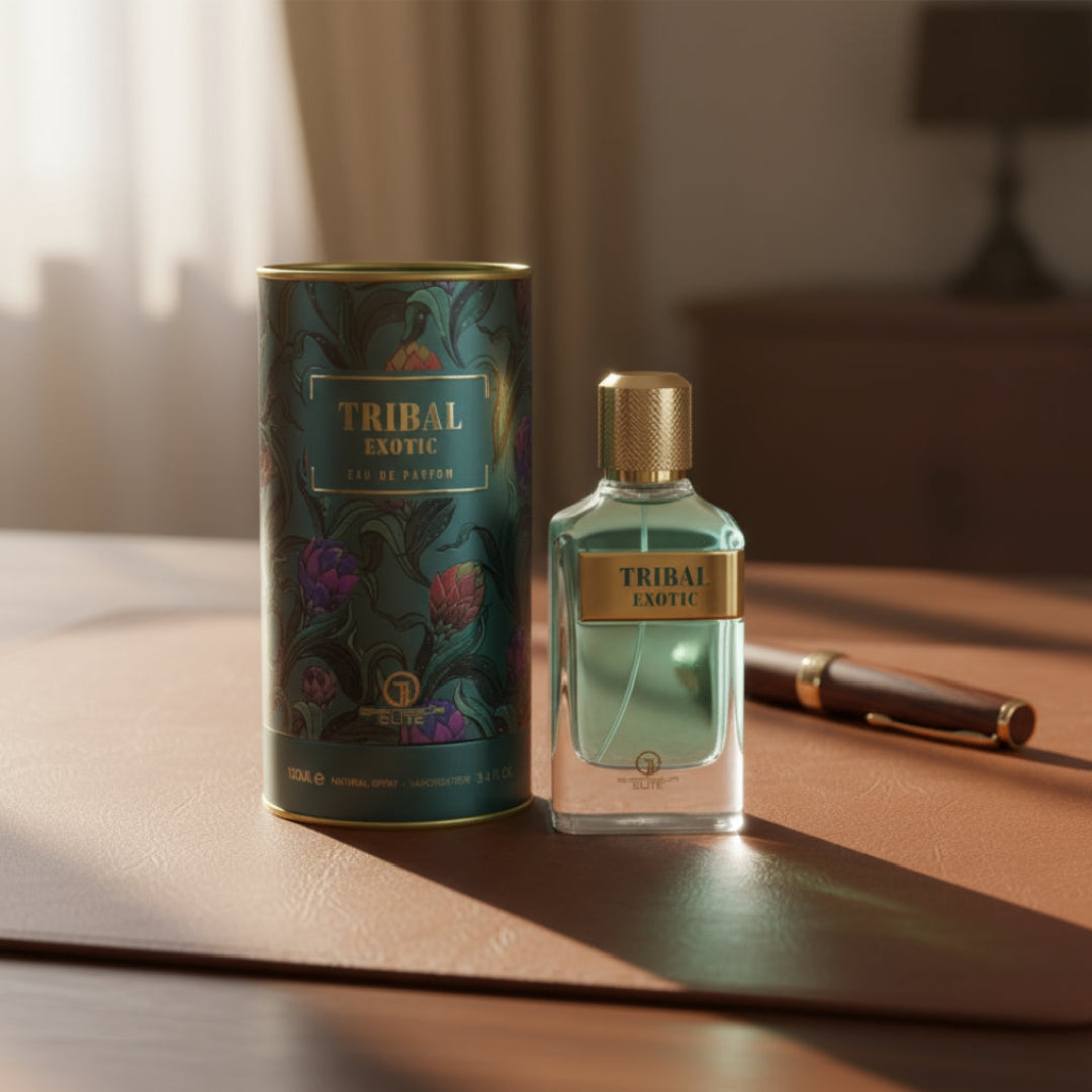 Grandeur Tribal Exotic by Grandeur 100ml EDP Men — A clear glass perfume bottle with a gold cap and a gold label reading 'TRIBAL EXOTIC' sits next to its matching cylindrical box with a dark green floral pattern. A brown fountain pen lies to the right.
