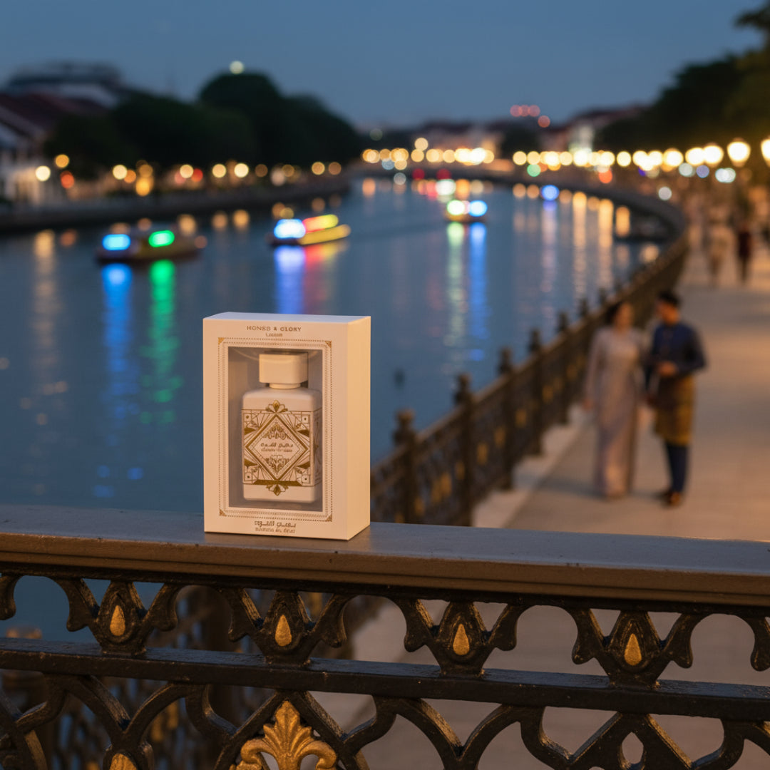 Lattafa Badee Al Oud Honor Glory — White perfume bottle in box on railing, river and city lights at dusk