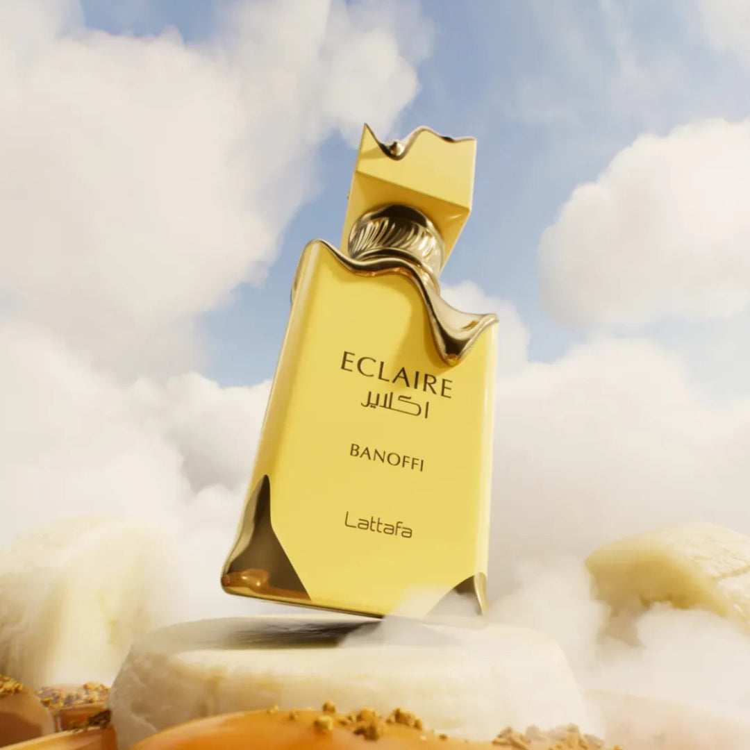 Lattafa Eclaire Banoffi — Yellow perfume bottle with gold accents, floating against a cloudy sky, on a pedestal with dessert