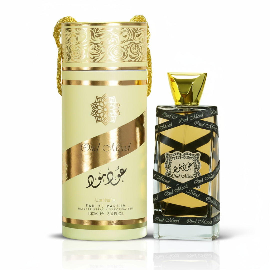 Lattafa Oud Mood Lattafa Arabian 100ml EDP — Cylindrical gold and cream gift box with ornate patterns and a gold drawstring, next to a clear glass perfume bottle with a gold cap, wrapped in black ribbon with repeated 'Oud Mood' text.