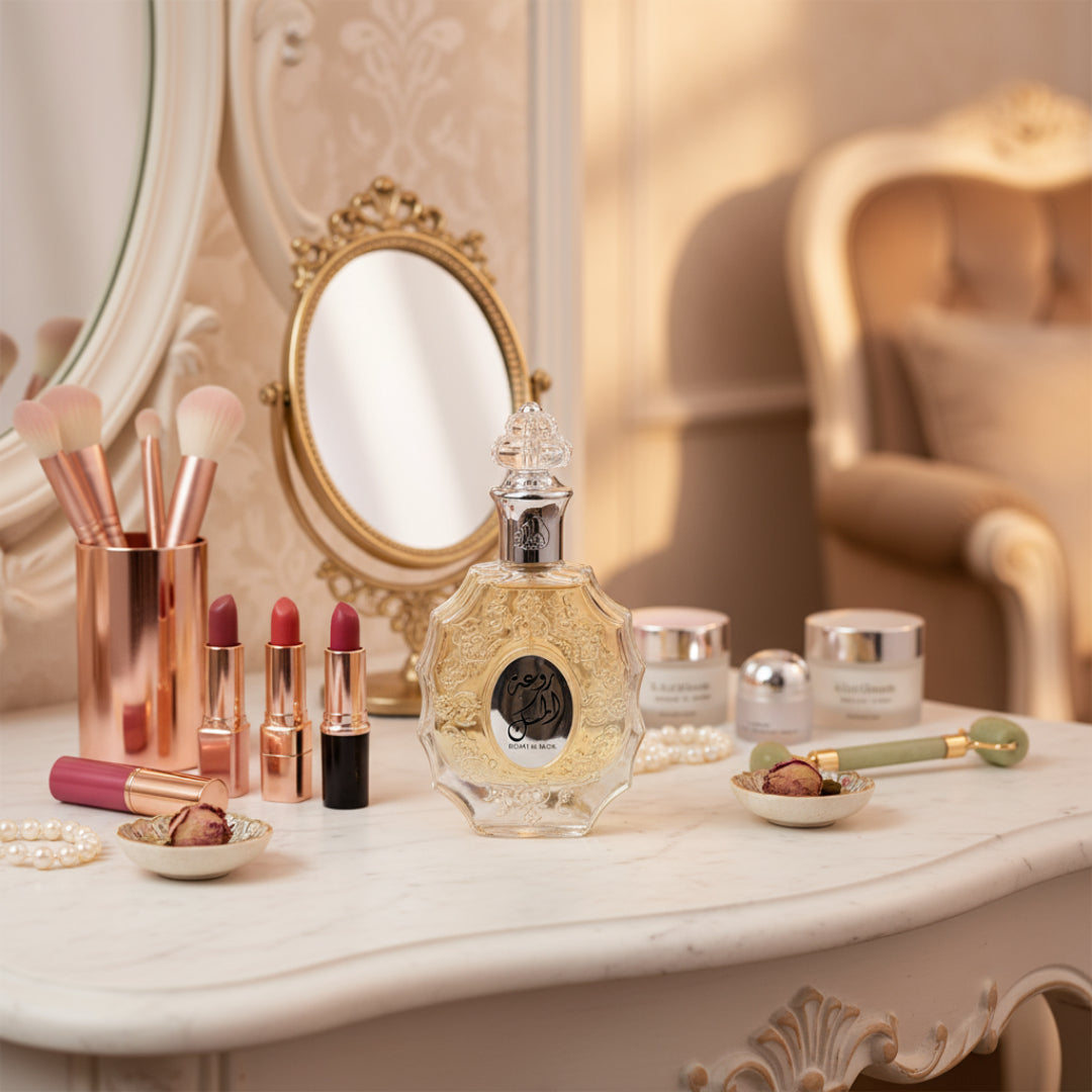Lattafa Rouat Al Musk by Lattafa 100ml for Women — A decorative perfume bottle with ornate gold detailing sits on a white marble vanity, surrounded by makeup brushes, lipsticks, skincare jars, and a jade roller.