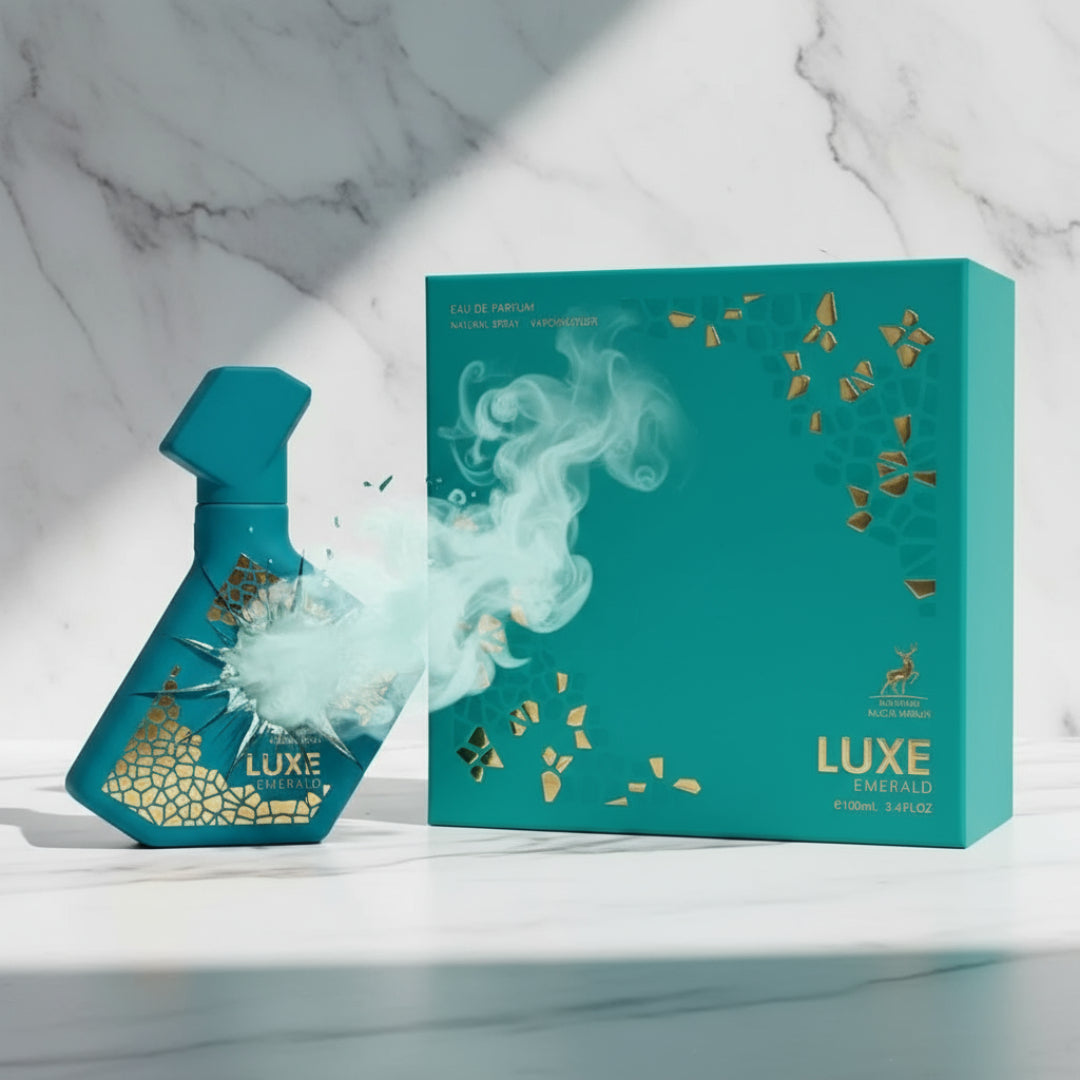 Maison Alhambra Luxe Emerald Perfume Maison Alhambra 100ml Unisex — Teal spray bottle with gold geometric pattern, releasing a cloud of mist, next to its matching teal gift box with gold accents, on a marble surface.