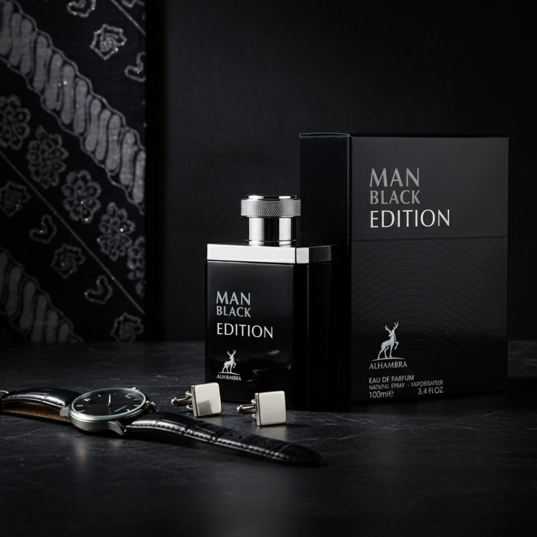 Maison Alhambra Man Black Edition — Black perfume bottle and box with silver cap, alongside a watch and cufflinks on a dark textured surface, with a patterned fabric in the background.