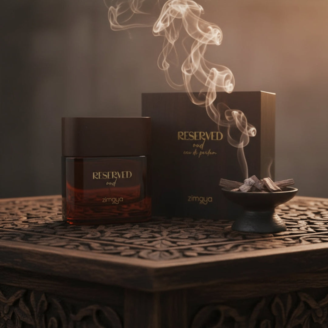 Zimaya Reserved Oud EDP 100 ml Unisex — A dark glass perfume bottle with a brown cap sits on a carved wooden table, with a matching box and a small dish of oud wood chips emitting smoke in the background.