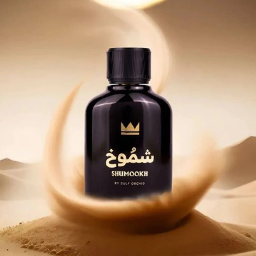 Gulf Orchid Shumookh Parfum 100ml by Gulf Orchid — A black perfume bottle with a gold crown logo and Arabic text, set against a desert-like background with swirling sand and soft golden light. | Gulf Orchid Shumookh Parfum 100ml by Gulf Orchid — Botol minyak wangi hitam dengan logo mahkota emas dan teks Arab, berlatar