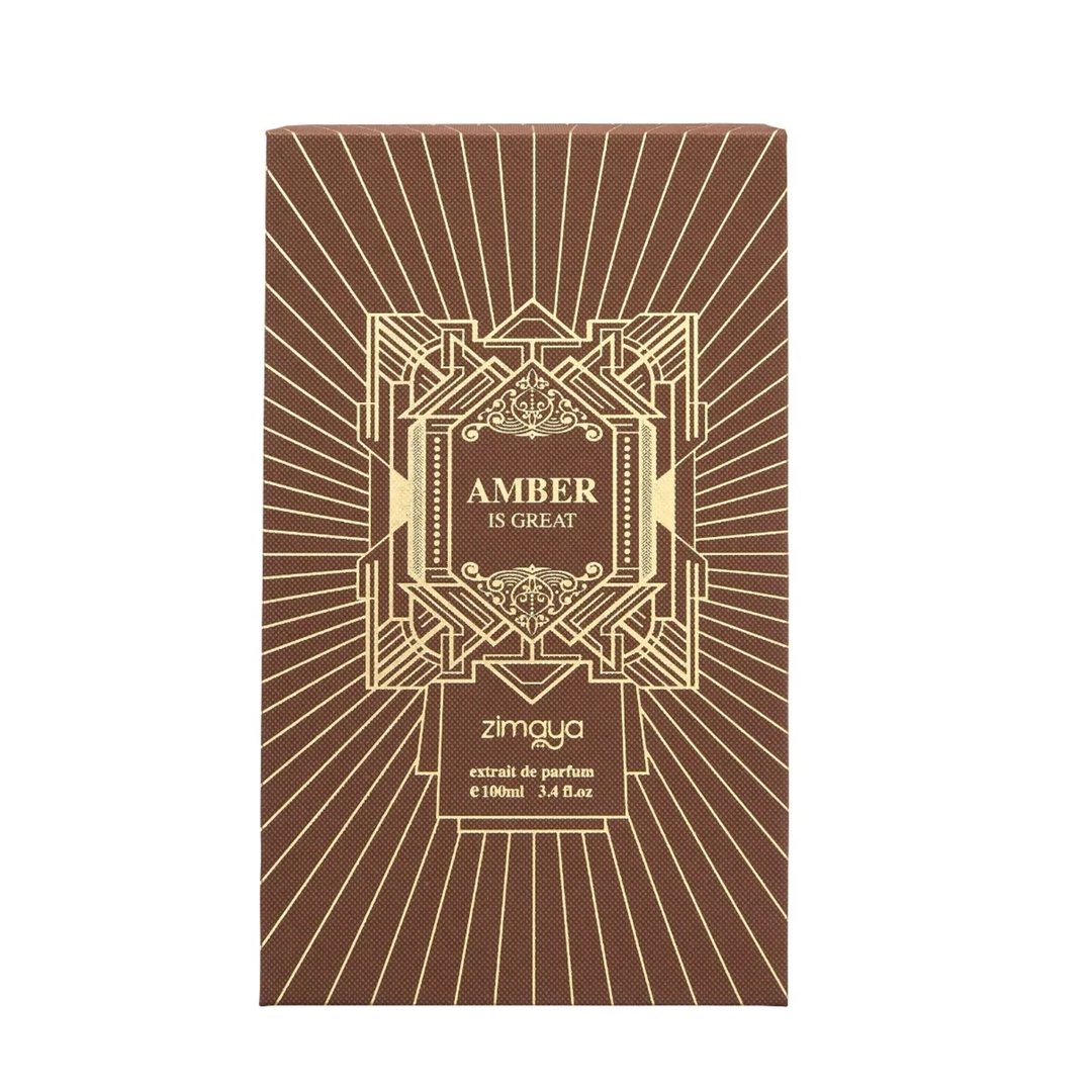 Zimaya Amber Is Great Eau De Parfum 100ml — A brown box with gold geometric patterns and sunburst lines, featuring the text "AMBER IS GREAT" in a central ornate frame, and "zimaya" logo below. | Zimaya Amber Is Great Eau De Parfum 100ml — Peti coklat dengan corak geometri emas dan garisan pancaran matahari