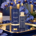 Maison Asrar Legacy by Maison Asrar 100ml EDP Unisex — Kotak silinder biru dan botol wangian Legacy by Maison Asrar bercorak senada dipamerkan di atas dulang emas dengan orkid biru dan lilin menyala di latar belakang.