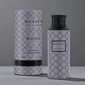 Majesty by Maison Asrar 100ml EDP Unisex — Kotak dan botol minyak wangi silinder bercorak geometri kelabu putih, penutup hitam pada botol, latar belakang kelabu.