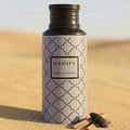 Majesty by Maison Asrar 100ml EDP Unisex — Botol kelabu cerah dengan corak geometri hitam dan penutup hitam, berdiri di atas pasir bersama beberapa ketul kayu gaharu dan sebiji buah pelaga gaharu di hadapan.