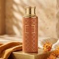 Monarch by Maison Asrar 100ml EDP Unisex — Botol minyak wangi tinggi berwarna terakota berhias corak geometri emas dan penutup bertekstur emas, dipamerkan di atas alas emas dengan fabrik jingga dan bunga kering.