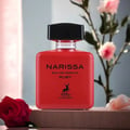 Maison Alhambra Narissa Ruby Eau de Parfum — A red perfume bottle with a black cap sits on a wooden surface, with a red rose in the foreground and pink flowers in the background. | Maison Alhambra Narissa Ruby Eau de Parfum — Botol minyak wangi merah dengan penutup hitam diletakkan di atas permukaan kayu, dengan mawar