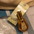 Ard Al Zaafaran Oud Mood by Ard Al Zaafaran 50ml EDP Unisex — A golden-capped glass perfume bottle with amber liquid sits next to its matching gold and white patterned box on a striped blue and beige background.