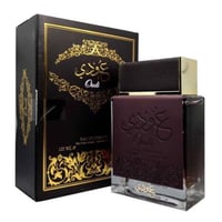 Ard Al Zaafaran Oudi Eau De Parfum 100ml — A brown perfume bottle with a textured cap and embossed Arabic calligraphy and 'Oudi' text, stands next to its matching dark brown box with gold ornate patterns and text. | Ard Al Zaafaran Oudi Eau De Parfum 100ml — Botol minyak wangi coklat dengan penutup bertekstur dan