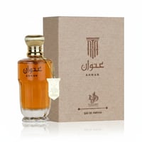 Al Wataniah Anwan Al Wataniah Woody For Her 100ml EDP — Amber glass perfume bottle with gold cap and tag next to a textured
