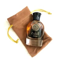 Al Wataniah Amnia — Amber perfume bottle with gold emblem and Arabic text, in a brown drawstring pouch.