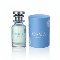 Osma Woody S Mango Leather 75ml EDP — A clear glass perfume bottle with a light green liquid and silver cap, next to a light blue cylindrical box with rose illustrations, both featuring the Osma Woody S logo.