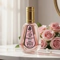 Ard Al Zaafaran Pink Blush Shams Al Emarat Khususi 50ml — A clear glass perfume bottle with pink liquid and a gold cap, set against a backdrop of pink roses and soft lighting.