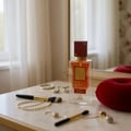 Perfume bottle on a table with makeup items and a red cushion in the background