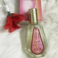 Al Rehab Sabaya by Al-Rehab 50ml EDP — A clear glass perfume bottle with a gold cap and a pink label sits on a white fluffy surface next to a red fabric flower and a pink box. | Al Rehab Sabaya by Al-Rehab 50ml EDP — Botol kaca jernih dengan penutup emas dan label merah jambu terletak di atas permukaan berbulu putih