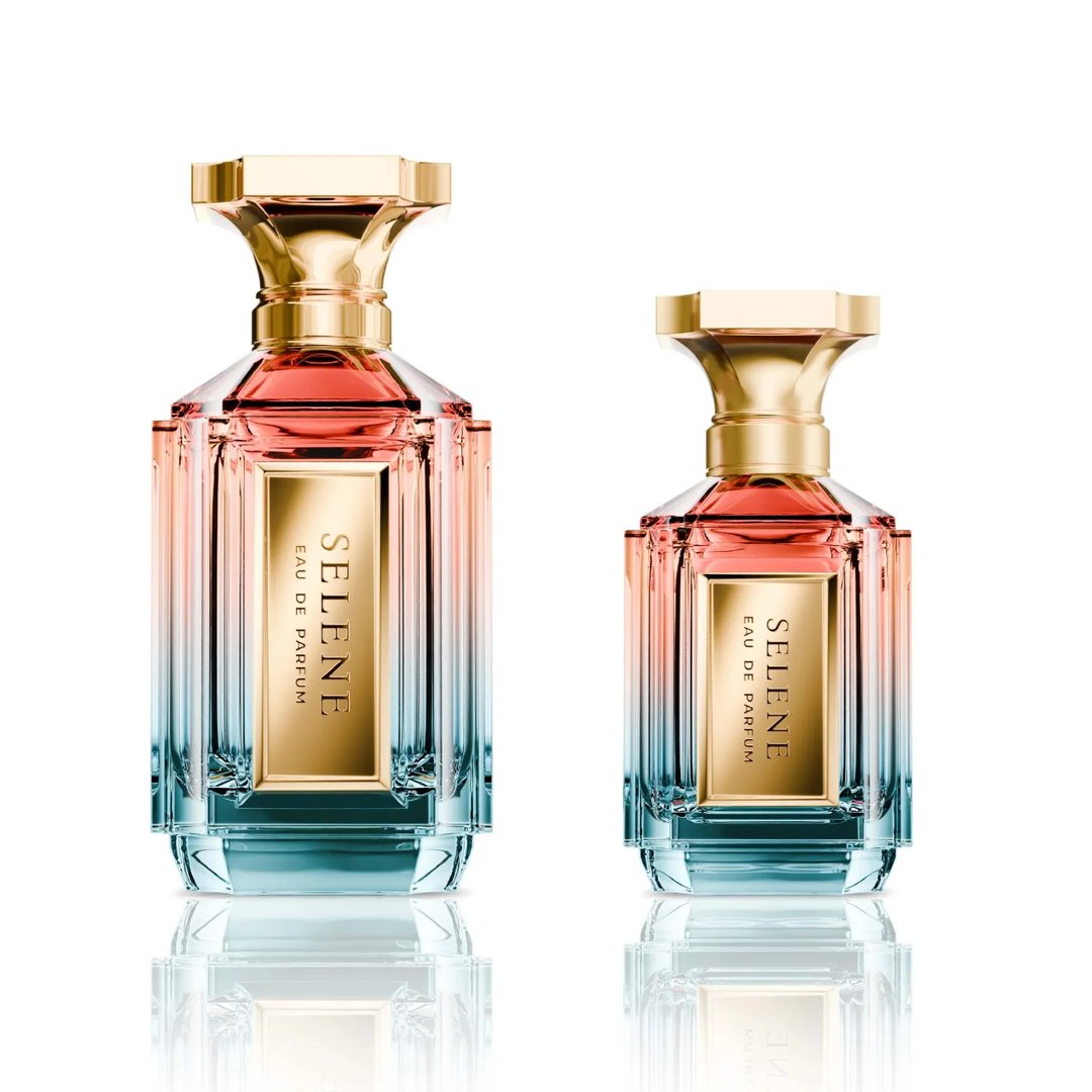 Velixir Selene Velixir Parfums 100ml — Two glass perfume bottles with gold caps and ombre pink to blue liquid, displayed side-by-side on a white reflective surface. | Velixir Selene Velixir Parfums 100ml — Dua botol minyak wangi kaca dengan penutup emas dan cecair ombre merah jambu ke biru, dipamerkan bersebelahan di