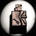 French Avenue Ghost Spectre — A rose gold, uniquely shaped perfume bottle with a bullet-like accent on the side and cap, illuminated by a spotlight against a dark background. | French Avenue Ghost Spectre — Botol minyak wangi berbentuk unik berwarna emas mawar dengan aksen seperti peluru di sisi dan penutupnya