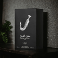 Lattafa Pride Ishq Al Shuyukh Silver — Black perfume box with a silver dagger illustration and Arabic text, set against a textured dark background with a hint of greenery.
