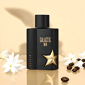 Maison Alhambra Galactic Man Elixir — Black perfume bottle with gold star emblem and "GALACTIC MEN" text, surrounded by white flowers and coffee beans on a reflective surface.