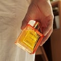Rayhaan Adonis Icarus Rayhaan Perfume 100ml — A hand holds a rectangular glass perfume bottle with orange-tinted glass and gold accents, filled with yellow liquid. | Rayhaan Adonis Icarus Rayhaan Perfume 100ml — Tangan memegang botol minyak wangi kaca berbentuk segi empat dengan kaca berwarna jingga dan perincian