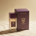 Bujairami Amber Eclipse by Bujairami 100ml Extrait — A clear glass perfume bottle with a textured pattern and a dark purple cap, placed next to its matching dark purple box on a sandy surface with sparkling gold dust in the background.