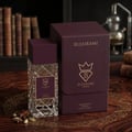 Bujairami Amber Eclipse by Bujairami 100ml Extrait — A clear glass perfume bottle with a textured diamond pattern and a deep purple cap, standing next to its matching deep purple presentation box. The box features a gold crown logo and brand name. The scene is set on a polished wooden surface with scattered star anise