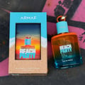 Armaf Beach Party Eau De Parfum 100ml — A blue and tan box with a beach sunset scene on the front is placed next to a gradient orange and blue glass perfume bottle with a light blue cap and orange ring | Armaf Beach Party Eau De Parfum 100ml — Kotak biru dan coklat dengan pemandangan matahari terbenam pantai di