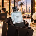French Avenue Arsh Black Ice — Clear glass perfume bottle with black cap and gold accent, displayed in a black gift bag with textured black paper lining, city skyline background.