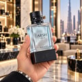 French Avenue Arsh Black Ice — Hand holding a clear glass perfume bottle with a black studded cap and gold accent, against a blurred luxury interior background with city skyline view.